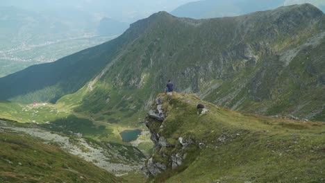 Totale-Aufnahme-Eines-Mannes,-Der-Auf-Einem-Riesigen-Felsen-Vor-Einem-Großen-Tal-Sitzt,-Mit-Den-Bergen-Im-Hintergrund