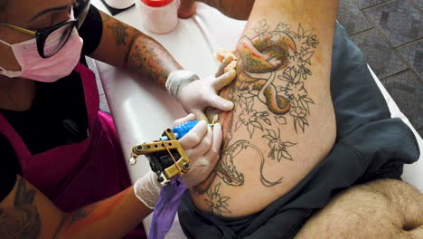 Tatuador-Con-Un-Escariador-De-Oreja-Pintando-Una-Serpiente-En-La-Pierna-Del-Hombre