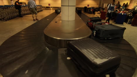 Airport-luggage-carousel,-conveyor-belt,-suitcases-and-luggage-moving,-passengers-waiting-and-looking-for-their-luggage-after-flight-arrival-in-airport-terminal,-bags-on-belt,-claim-baggage