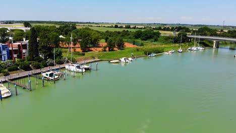 Boats-and-beach-homes-line-the-pier-entrance-to-the-harbor-while-a-small-boat-exits,-Aerial-drone-flyover-shot