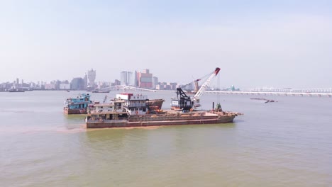 Drohnen-Orbitaufnahme-Von-Greifbaggern-Und-Trichterschiffen-Mit-Sicht-Auf-Die-Skyline-Der-Stadt-Macau-Im-Hintergrund