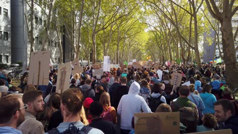 Huge-crowd-of-students,-teenagers-and-other-protsters-march-down-a-boulevard-with-trees,-to-demand-political-action-against-global-warming