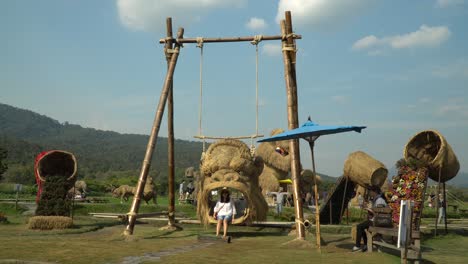 Fun-on-a-King-Kong-head-swing-at-the-Straw-sculptures-park-in-Chiang-Mai,-Thailand-surrounded-by-a-beautiful-landscape-and-lush-green-mountains