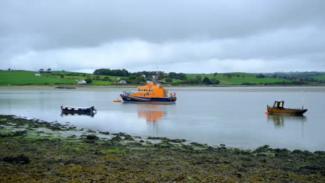 Bote-Salvavidas-Rnli-Amarrado-Con-Otros-Botes-Pequeños-Durante-La-Marea-Baja-Y-El-Océano-En-Calma-En-El-Condado-De-Cork,-Irlanda