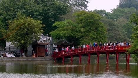 El-Puente-Rojo-Huc-También-Llamado-El-Puente-Del-Sol-En-El-Templo-Ngoc-Son-Con-Turistas-Cruzándolo,-Bloqueando-El-Tiro-De-Establecimiento