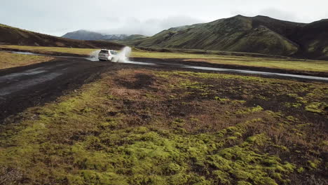 Aerial-Action-View-of-Four-Wheel-SUV-Vehicle-on-Muddy-Road-Crossing-Small-River-in-Iceland-Countryside