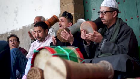 Low-angle-shot-of-gathering-of-men-in-traditional-clothing-chanting-and-hitting-drums-going-into-a-trance-during-a-sufi-ceremony