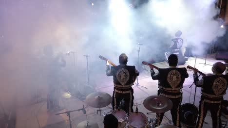 Wide-angle-shot-from-behind-Mariachi-band-on-stage-with-large-audience-and-smoke-pouring-out-in-Merida,-Mexico