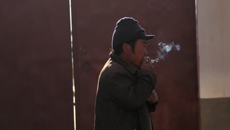 Hombre-Fumando-Cigarrillo-En-La-Mañana-Soleada-En-El-Mercado-Al-Aire-Libre-De-La-Aldea-Shaxizhen-Shaxi