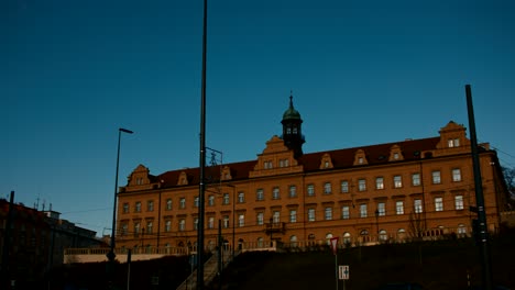 Zeitraffer-Des-Rangherka-Gebäudes-Im-Stadtteil-Vrsovice-Am-Herbstmorgen-Mit-Vorbeifahrenden-Straßenbahnen,-Menschen-Und-Autos