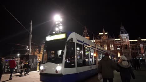 Amsterdamer-Dammplatz-Und-Hauptbahnhof-Während-Des-Silvesterabends-Mit-Vorbeifahrenden-Menschen-Und-Straßenbahnen