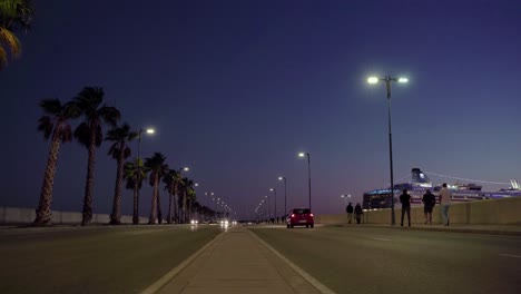 Tourists-walking-on-the-side-of-Paseo-de-la-Farola-in-Malaga,-next-to-harbor