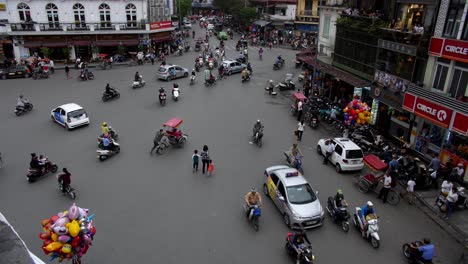 Busy-intersection-with-taxis,-cyclos,-cars,-and-people-crossing-at-the-same-time-during-the-day,-high-angle-stable-shot