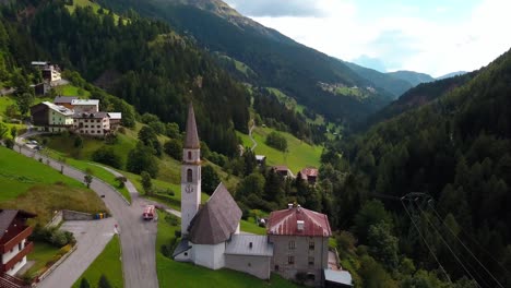 Pueblo-Con-Carretera-E-Iglesia-En-La-Zona-Montañosa-Con-Casas-Y-Chalés,-Toma-Aérea-De-órbita-De-Drones