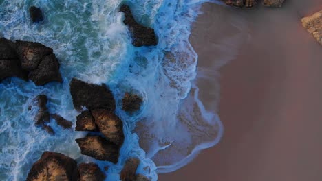 Beautiful-aerial-drone-overhead-rotating-shot-of-waves-crashing-the-rocky-beach-shore
