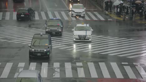 Coches-Y-Taxis-Conduciendo-Por-La-Carretera-Mojada-En-El-Cruce-De-Shibuya-En-Tokio-En-Un-Clima-Lluvioso---Hora-Punta---ángulo-Alto,-Tiro-De-Tele