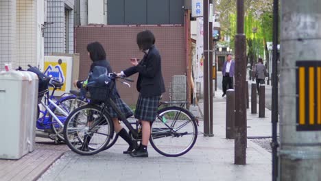 Niñas-Japonesas-Felices-En-Uniforme-Escolar-Charlando-En-Sus-Bicicletas---Tiro-En-Cámara-Lenta