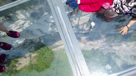 People-walking-and-sitting-on-the-transparent-glass-viewing-platform-installed-above-gorge-valley-surrounded-by-karst-limestone-rock-formations-in-Wulong-National-Park,-China