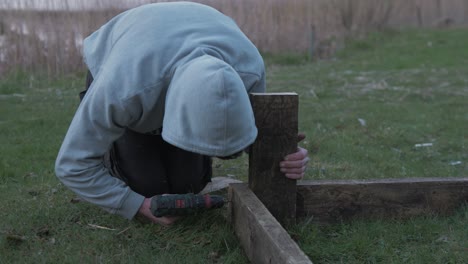 Young-carpenter-wood-working-drilling-planks-together-raised-garden-bed-MID-SHOT