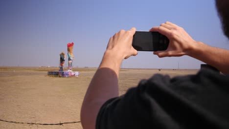 Tourist-takes-a-picture-of-the-Ozymandias-on-the-Plains-statue-in-Amarillo-Texas