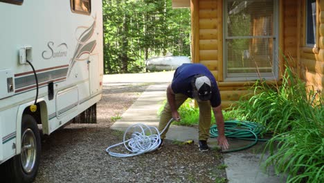 A-man-connects-hoses-on-the-side-of-a-house-and-a-RV