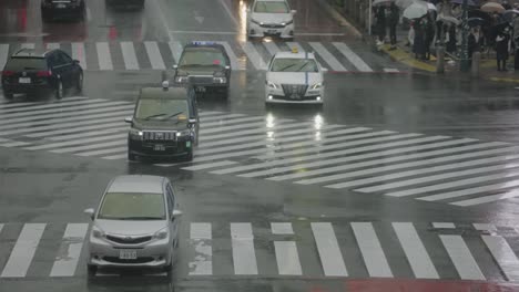Escena-De-Tráfico-En-El-Cruce-De-Shibuya-En-Tokio,-Japón-En-Un-Día-Lluvioso---Taxis-Moviéndose-En-Cámara-Lenta---Tiro-De-Tele