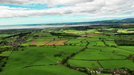 Aerial-tracking-shot-of-the-landscape-of-the-lush-green-countryside-on-the-coastline,-bright-sunny-day