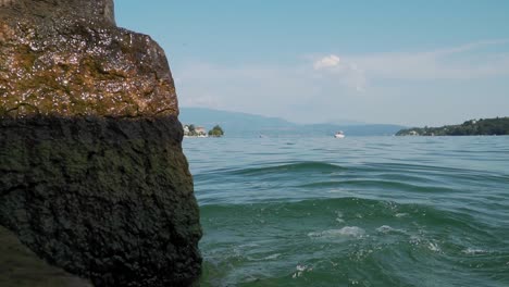 Lake-water-waves-splashing-on-stone-close-up,-view-from-shore,-lakeside-panorama