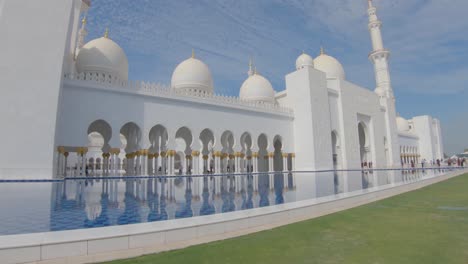 Visitors-by-entrance-to-Grand-Sheikh-Zayed-Mosque,-hallway-with-reflection-pool