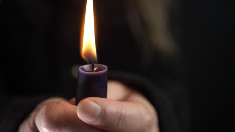 Woman-holding-a-long-candle-for-vigil-on-dark-background-close-up-shot