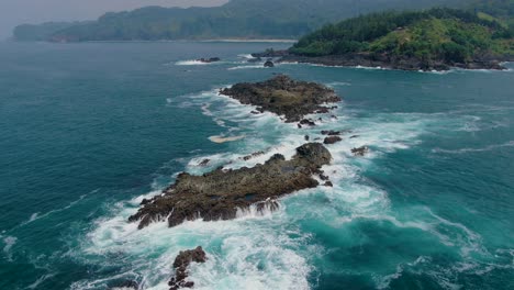 Aerial,-Indian-Ocean-calm-waves-splash-on-rocky-coast-of-Java-island,-Indonesia