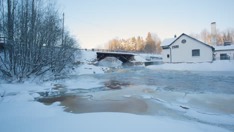 Static-view-of-house,-bridge,-snow-and-icy-river-in-wintertime-Finland