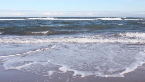 Low-angle-shot-of-waves-splashing-on-sandy-shore-during-sunny-day-with-horizon-in-background