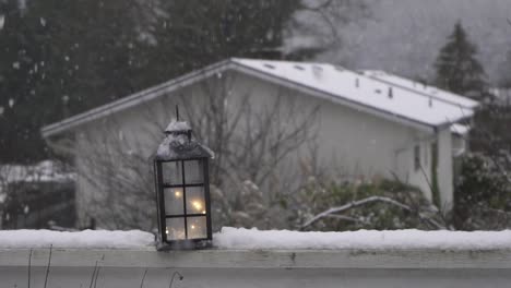 Electric-lantern-shining-bright-during-winter-as-snowfall-covers-the-brush,-rooftops,-and-mountain-ranges-in-Canada