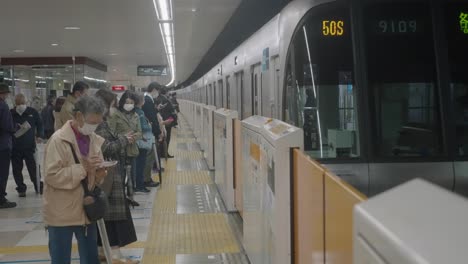 Der-Jr-Zug-Nähert-Sich-Dem-Bahnhof,-Während-Menschen-Mit-Gesichtsmasken-Auf-Dem-Bahnsteig-Stehen-Und-Warten-–-Ausbruch-Der-Coronavirus-Pandemie-In-Tokio,-Japan