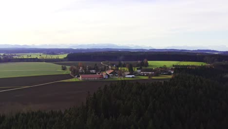 Zeitraffer-Eines-Idyllischen-Dorfes-Hinter-Einem-Wald-Vor-Den-Alpen-Im-Hintergrund