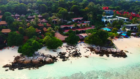 An-aerial-shot-of-a-resorts-by-the-beach-with-few-unrecognisable-people-walking-along-the-shoreline-and-trees-in-the-background