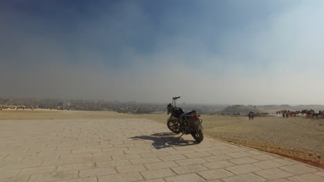 Cámara-Yendo-Hacia-Una-Moto-Parada-Frente-A-Una-Asombrosa-Vista-Panorámica-Del-Desierto-Egipcio-Durante-Un-Día-Soleado-En-Giza