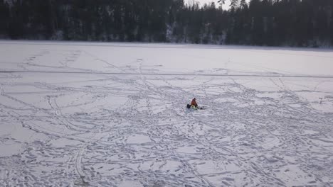 Reverse-tracking-shot-of-lonely-fisherman-patiently-waiting-next-to-his-hole-in-the-ice-for-anything-to-bite