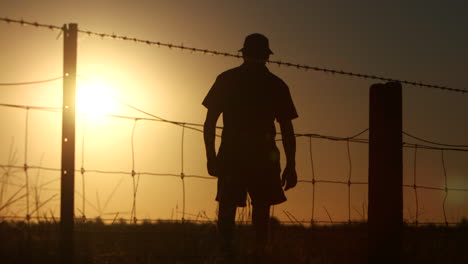 Silhouette-of-farmer-walking-away-wire-fence