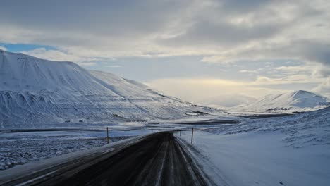 Driving-along-a-deserted,-snow-covered,-mountain-road-in-Iceland-under-the-midnight-sun