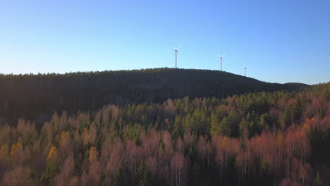 Aerial-drone-view-over-leafless-trees-and-a-hill,-heading-towards-a-wind-power-generator-turbine,-on-the-top-of-a-mountain,-in-Hoga-kusten,-Vasternorrland,-Sweden