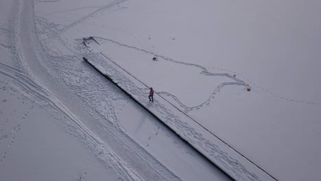 Zoom-out-aerial-footage-showing-woman-walking-on-a-frozen-jetty-towards-the-end-of-the-pier