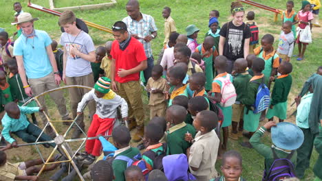 Afrikanische-Kinder-Spielen-Auf-Einem-Spielplatz,-Während-Sie-Draußen-In-Ihrer-Grundschule-Sind,-Während-Einige-Amerikanische-Besucher-Daneben-Stehen,-Zeitlupe