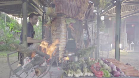 Toma-Manual-En-Cámara-Lenta-De-Un-Chef-Agregando-Carbón-A-La-Chimenea-Cocinando-Verduras-Y-Carne-A-La-Parrilla-En-Una-Típica-Barbacoa-Argentina-Llamada-Asado