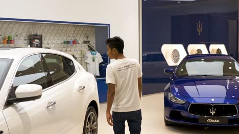 Junger-Asiatischer-Mann-Geht-In-Das-Luxus-Einkaufszentrum-Maserati-Händler,-Um-Sich-Die-Auswahl-An-Fahrzeugen-In-Icon-Siam,-Bangkok,-Thailand-Anzusehen