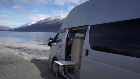 Motorhome-by-beautiful-blue-Lake-Wakatipu,-Queenstown,-New-Zealand-with-mountains-fresh-snow-cloudy-sky-in-background