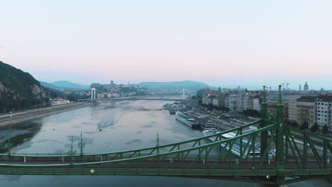 Luftdrohnenaufnahme-Eines-Bootes-Auf-Der-Donau-In-Budapest-Bei-Sonnenaufgang,-Morgen,-Mit-Freiheitsbrücke-Im-Vordergrund