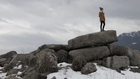 A-girl-stands-on-boulders-with-snowy-mountains-around-her