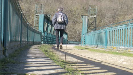 An-adult-man-with-backpack-walking-over-the-big-iron-bridge-with-blue-fence-on-a-bright-sunny-day